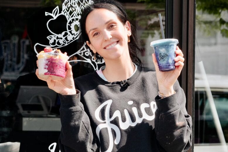 A smiling Arielle Cassidy holds a smoothie in one hand and a smoothie bowl in another at the Juice House in New Jersey