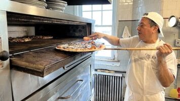 Man with pizza in front of oven at Conte's Pizza in Princeton