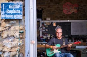 Craftsman Curt Wilson sits with a guitar at the entrance of his Old School Guitar–Repair, Restoration and Lutherie in Hopewell