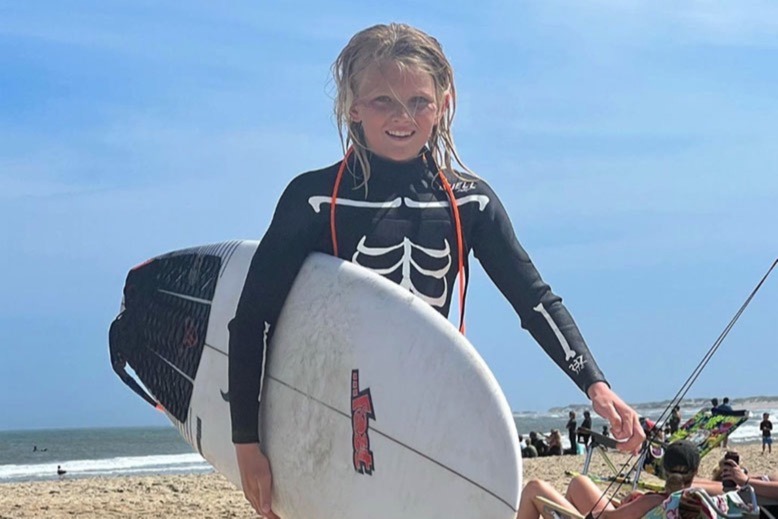 Carter Doorley carries a surf board on the beach