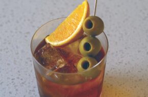 Glass of vermouth garnished with an orange wedge and olives