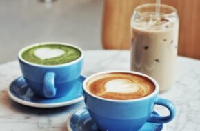 Two hot lattes in blue mugs and an iced coffee beverage in a clear glass