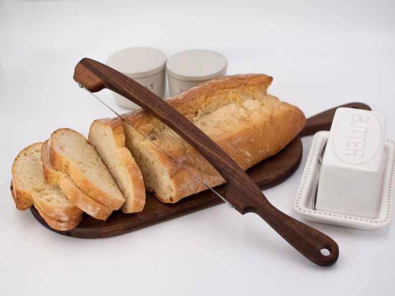 Bread bow knife and a loaf of bread atop a wooden board