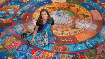 Artist Siona Benjamin sits on the tile mosaic she created.