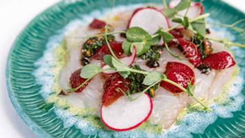 A dish of fresh seafood topped with strawberry and radish slices