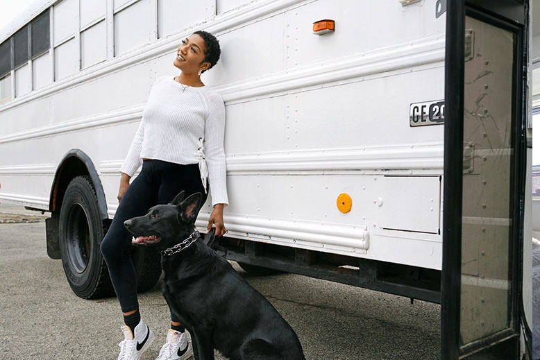 Tyler and her dog outside her white school-bus home