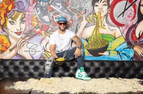 Chef Robbie Felice poses with a bowl of ramen at a table covered with ramen noodles at Pasta Ramen in Montclair