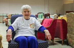 Maryjo Welch sitting in a chair, surrounded by furniture for nonprofit Interfaith Furnishings in Morris County