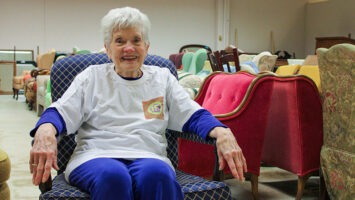 Maryjo Welch sitting in a chair, surrounded by furniture for nonprofit Interfaith Furnishings in Morris County