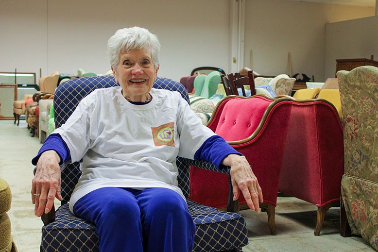 Maryjo Welch sitting in a chair, surrounded by furniture for nonprofit Interfaith Furnishings in Morris County