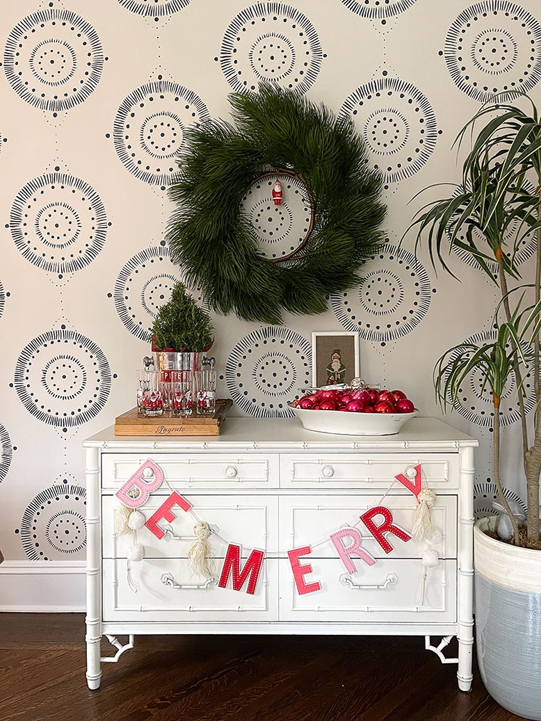 A white dresser adorned with a hanging "Be Merry" sign