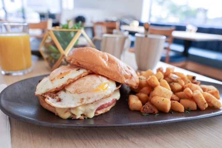 A breakfast sandwich, home fries and a glass of orange juice