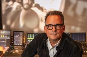 Thom Zimny, Bruce Springsteen's longtime filmmaker, sits in a production studio with archival footage of Springsteen behind him