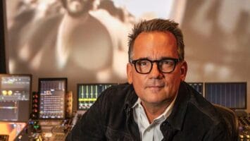 Thom Zimny, Bruce Springsteen's longtime filmmaker, sits in a production studio with archival footage of Springsteen behind him