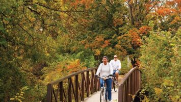 bikers on a wooden bridge in a park with fall foliage