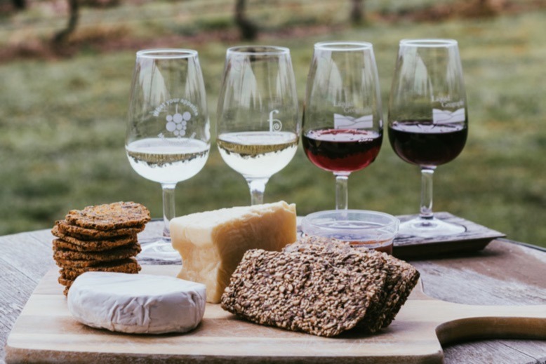 Assortment of red and white wines behind a platter of assorted cheeses and crackers