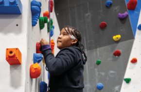 young child climbing a wall with colorful foot and hand holds