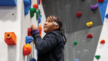 young child climbing a wall with colorful foot and hand holds