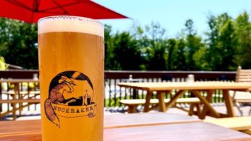 Muckraker Beermaker's Insalata ale on an outdoor table with an umbrella and trees in the background