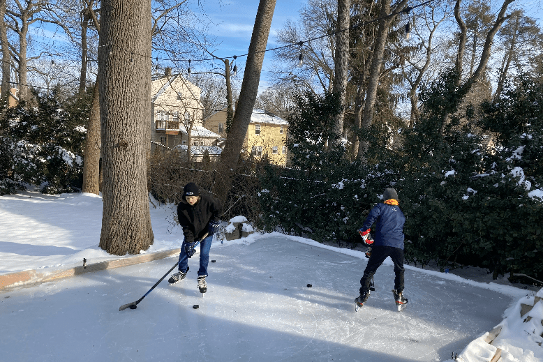 Two young boys play ice hockey on their backyard skating rink in Montclair