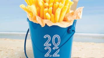 Fries in a bucket sitting on a beach.