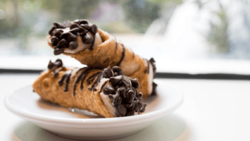 Two cannolis on a plate by a window