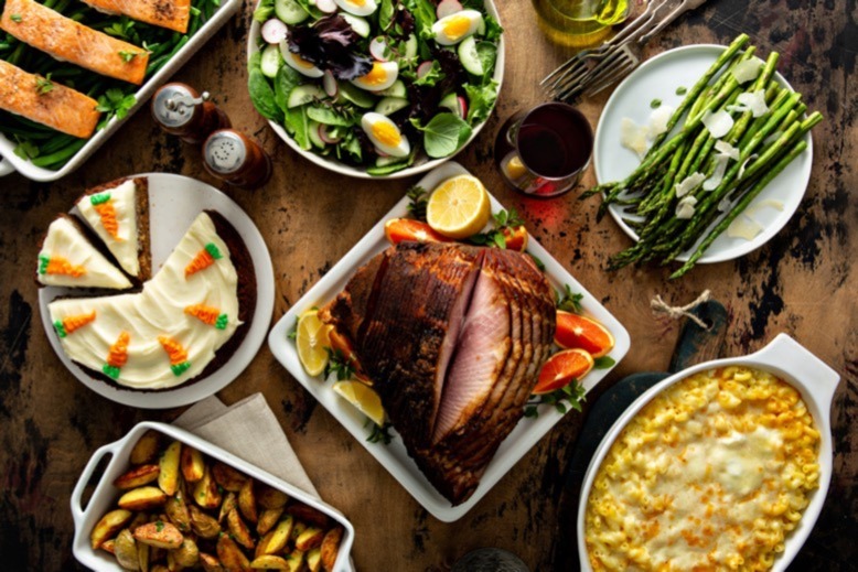 A table with plates of foods like ham, asparagus, macaroni and cheese, salmon, salad and carrot cake