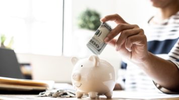 Person putting folded up $100 bill into piggy bank