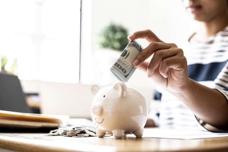 Person putting folded up $100 bill into piggy bank