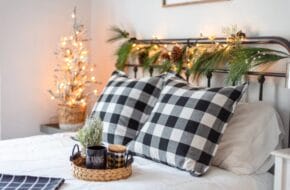 Made bed with Christmas decorations on the headboard and nightstand, and a tray with a coffee mug