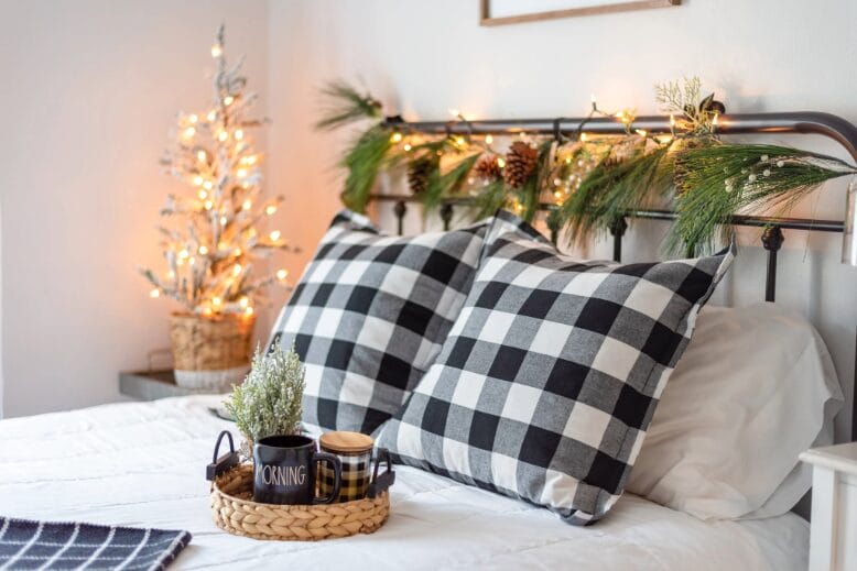 Made bed with Christmas decorations on the headboard and nightstand, and a tray with a coffee mug