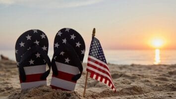 American flag and American flag flip-flops in sand at beach at sunset