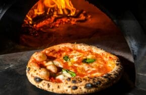 Pizza coming out of wood-burning oven