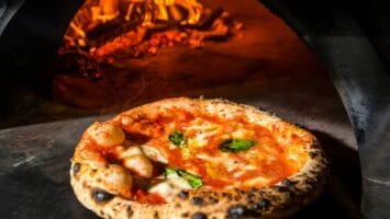 Pizza coming out of wood-burning oven