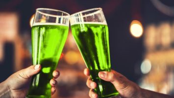 Two friends toast glasses filled with green beer.