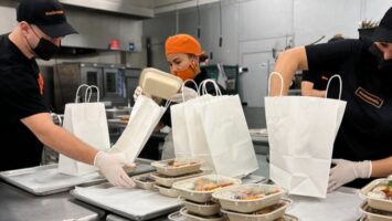 Three employees packing meals in a kitchen