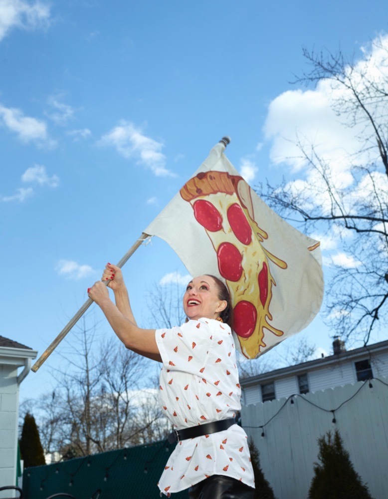 Telina Cuppari, wearing a pizza-print shirt, waves a giant pizza glass outside her Kenilworth home