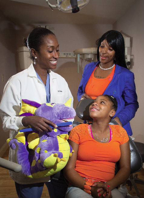 Dr. McGrath shows Karen and mother Kyisha Branch the proper brushing technique using Prince, a purple dragon. Photo by Andy Foster