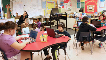 Teacher Lei Han Hong, left, leads a small group of Normandy Park Elementary School students in traditional learning, while others work individually on their laptops.