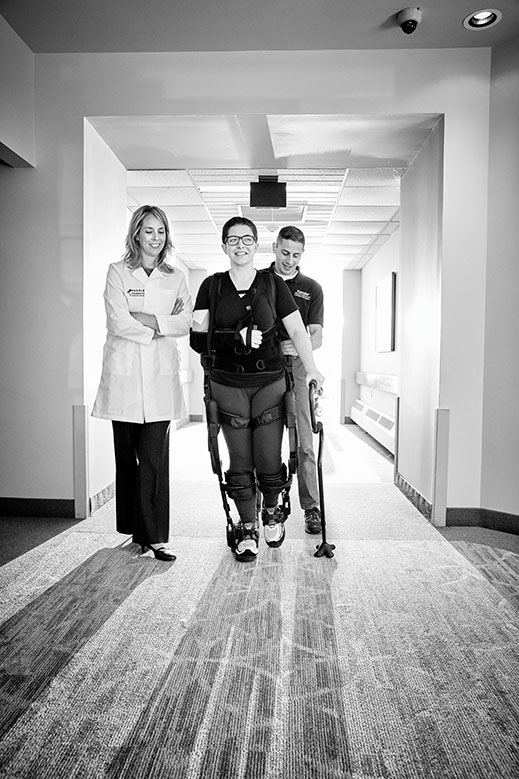 Assisting with her therapy are senior research scientist Karen Nolan and therapist Adam Kesten. The Ekso allows Yurek to practice the complicated sequence of neuromuscular actions involved in walking.