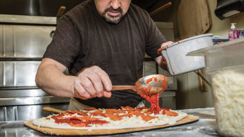 At Papa’s, cook Antonio Gonzalez spoons chunky plum tomato sauce on a pie.