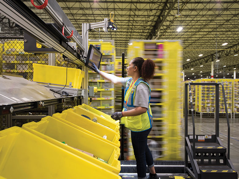 A picker sticks to her workstation at the Carteret fulfillment center while a robot roams the aisles grabbing the pods needed to fulfill yet another Amazon order.