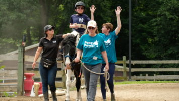 A child rides a horse with the help of employees at Pony Power Therapies