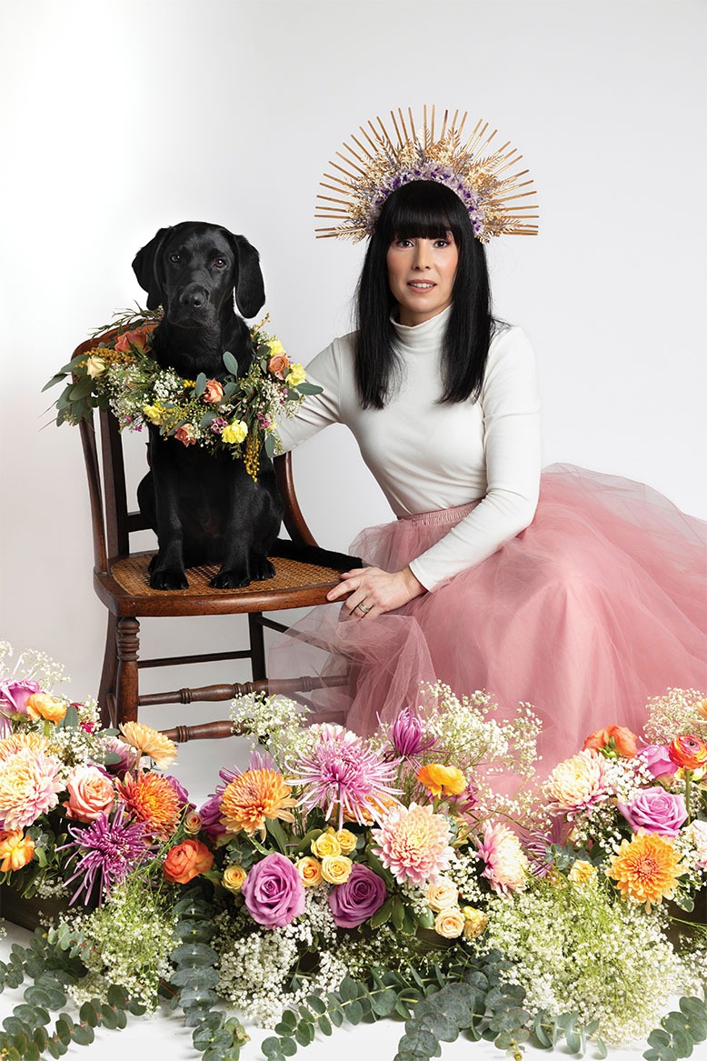 Photographer Stephanie Blum poses for a self-portrait, with photogenic pup Jay, among colorful florals