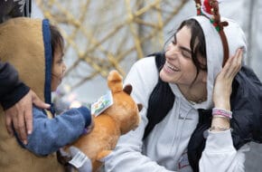 Woman with reindeer ears talks to young child holding stuffed animal