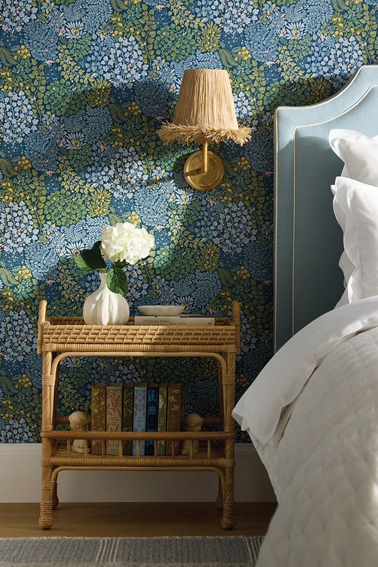 Bedroom with rattan side table, blue and green wallpaper, and white bedding