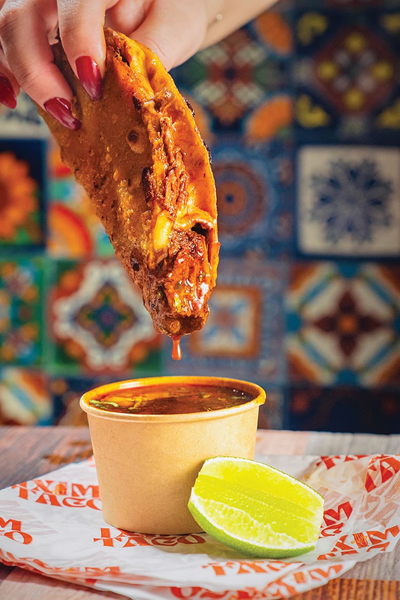 Birria taco being dipped into broth at Bitol in Clifton, NJ