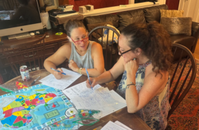 Two Montclair moms working at a table on their board game, "Dad in Chad"