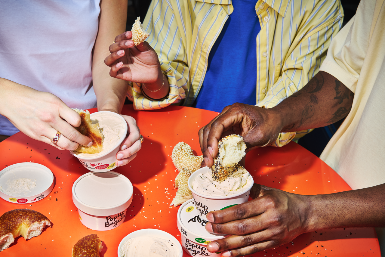 People dipping PopUp bagels in cream cheese