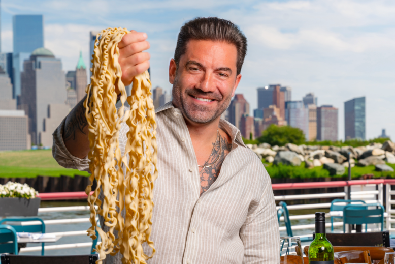 Chef Ryan DePersio holds up a fistful of pasta outside his restaurant Battello in Jersey City, NJ, with the Manhattan skyline behind him